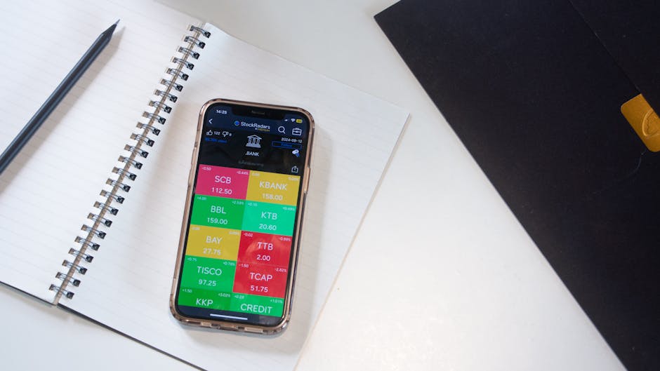 A smartphone displays a financial stock market app on a desk with a notebook and pencil